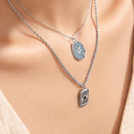Model wearing layered starburst and square pendant necklaces in polished 316L stainless steel