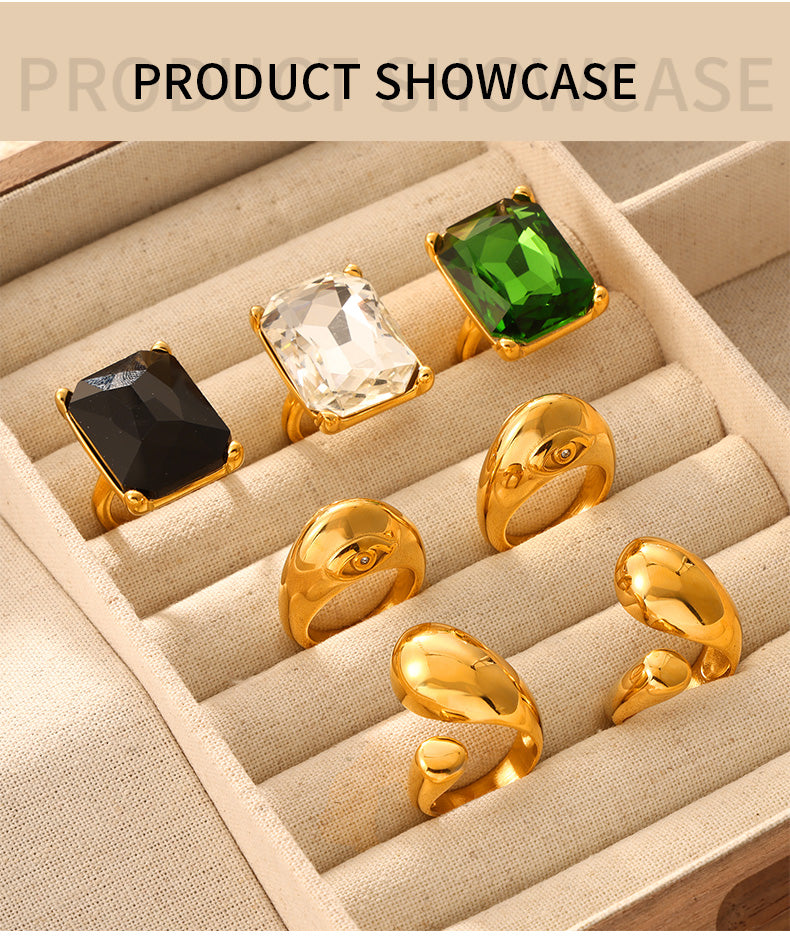 Product showcase of rectangular stone rings and gold-tone sculptural rings in a jewelry box