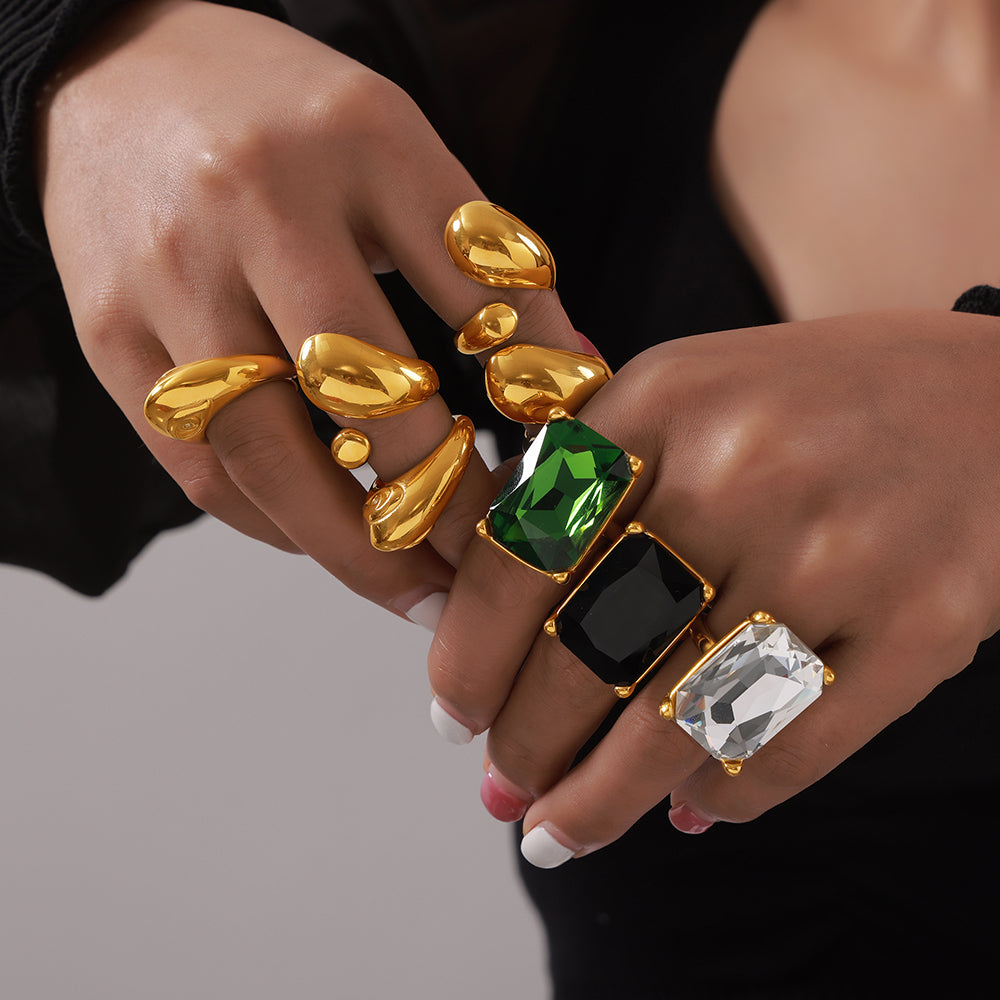 Model wearing gold-tone sculptural rings and clear, black and green rectangular stone cocktail rings
