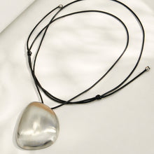Polished steel pebble pendant necklace with a long black cord arranged in a flat lay