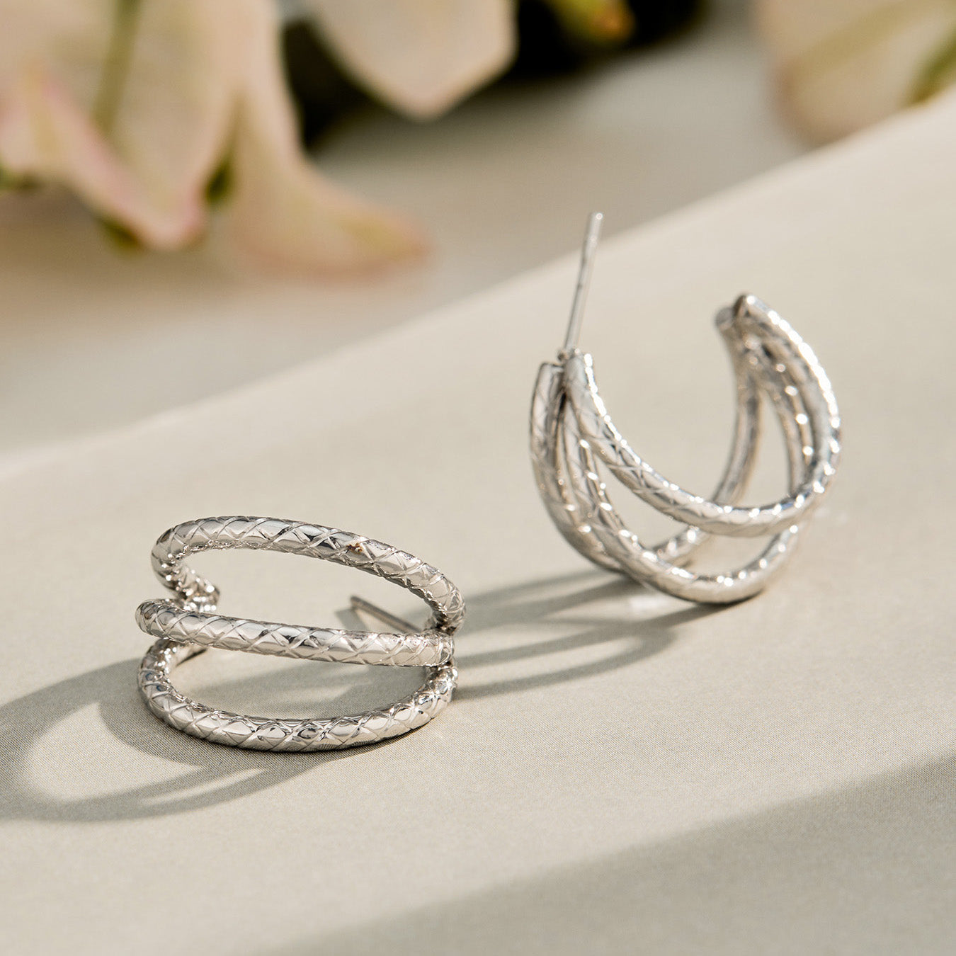 Steel-tone chunky double layer hoop earrings displayed on a neutral reflective surface