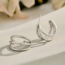Steel-tone chunky double layer hoop earrings displayed on a neutral reflective surface