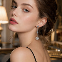 Steel-tone clover drop earrings with white crystals worn by a model