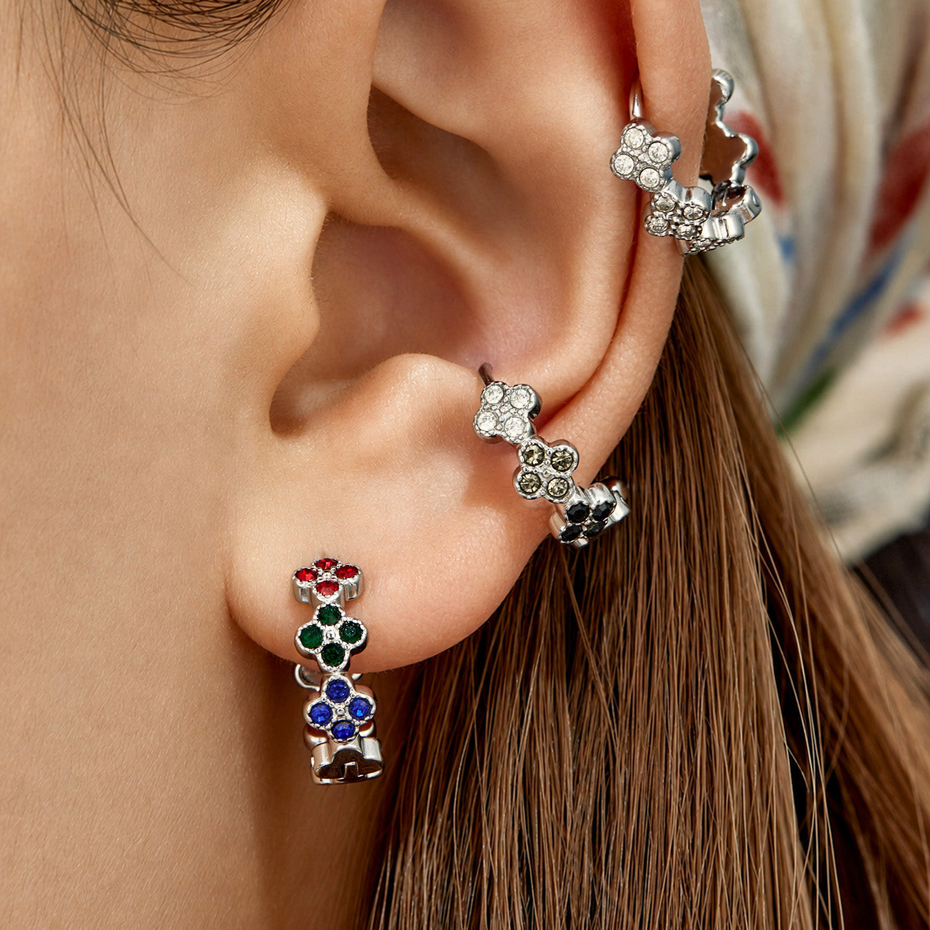 Model wearing steel-tone clover huggie earrings with multicolor cubic zirconia