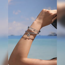Close-up of a gold-tone nail bangle bracelet layered with slim bangles in a seaside setting
