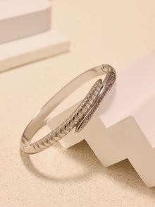 Steel-tone nail bangle bracelet with pink zircon accents displayed on white geometric blocks