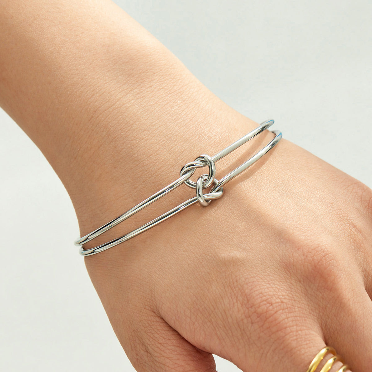 Steel-tone double wire knot open bangle worn on a model's wrist