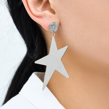 Steel-tone stainless steel statement star drop earrings worn on ear
