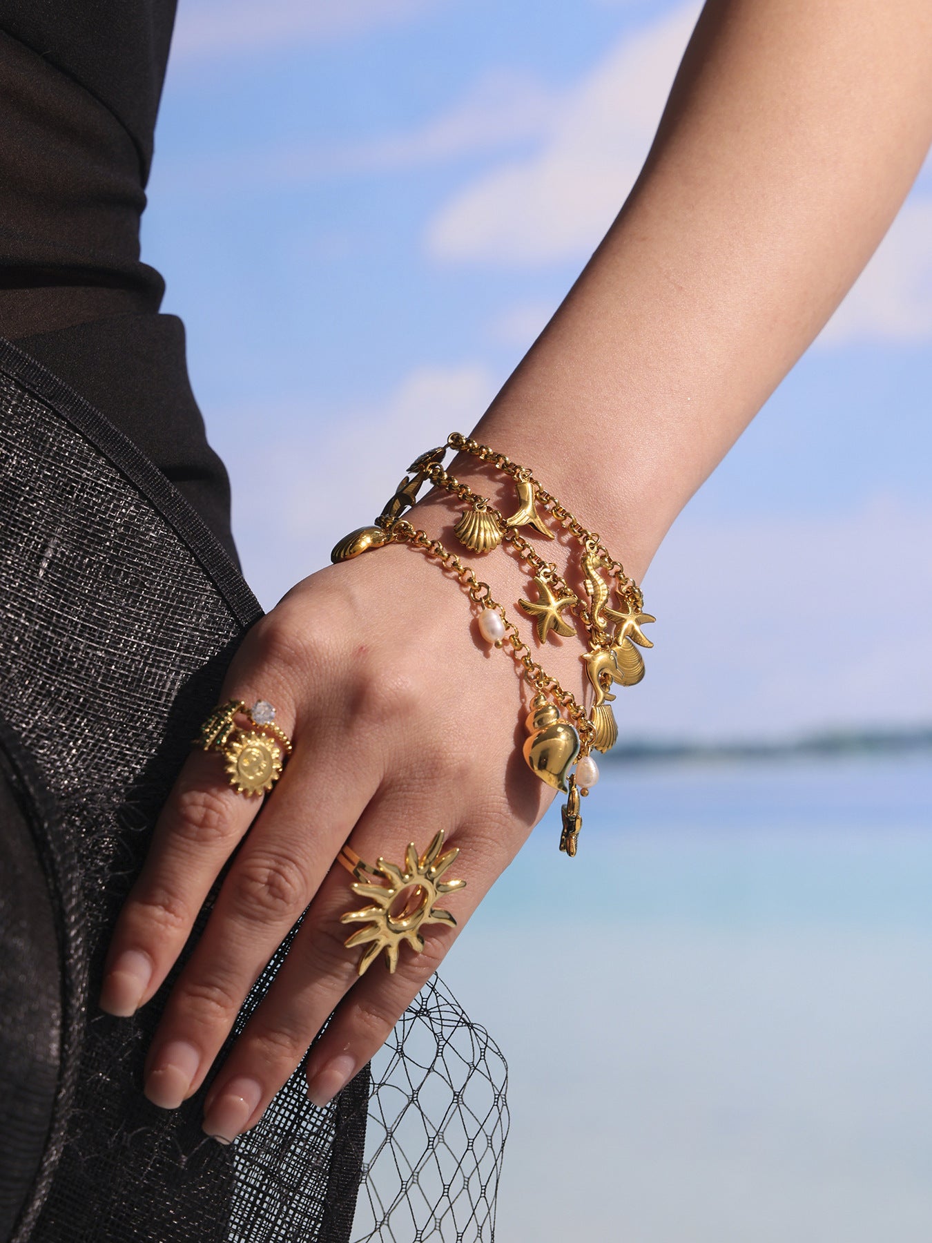 Close-up beach styling of layered shell pearl charm bracelets and matching anklet, waterproof 18K PVD gold jewelry set