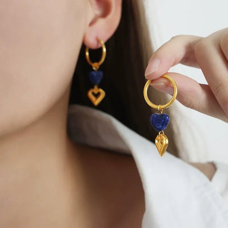 Close up of hand holding tarnish-free romantic jewelry featuring 18K gold heart drop huggie earrings.