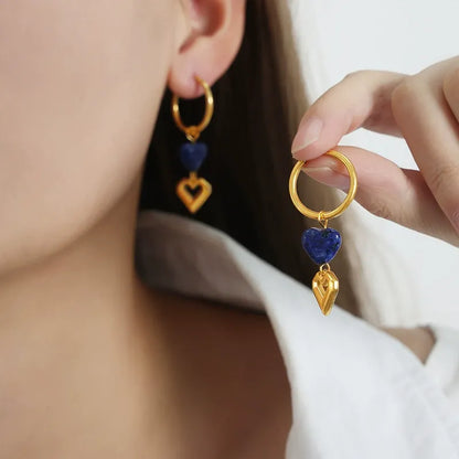 Close up of hand holding tarnish-free romantic jewelry featuring 18K gold heart drop huggie earrings.