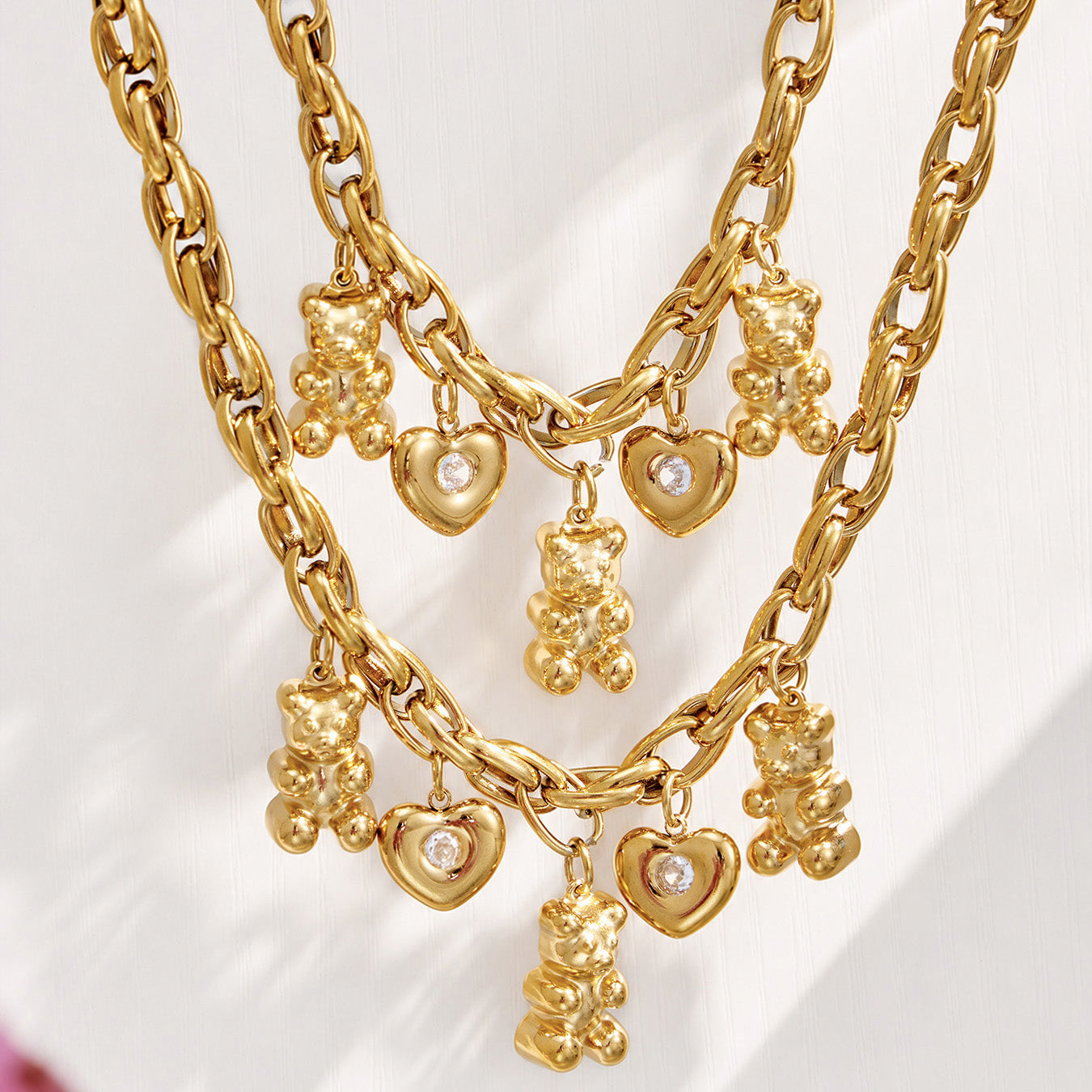 Close-up of teddy bear, open heart and clear zircon charms on a gold link chain