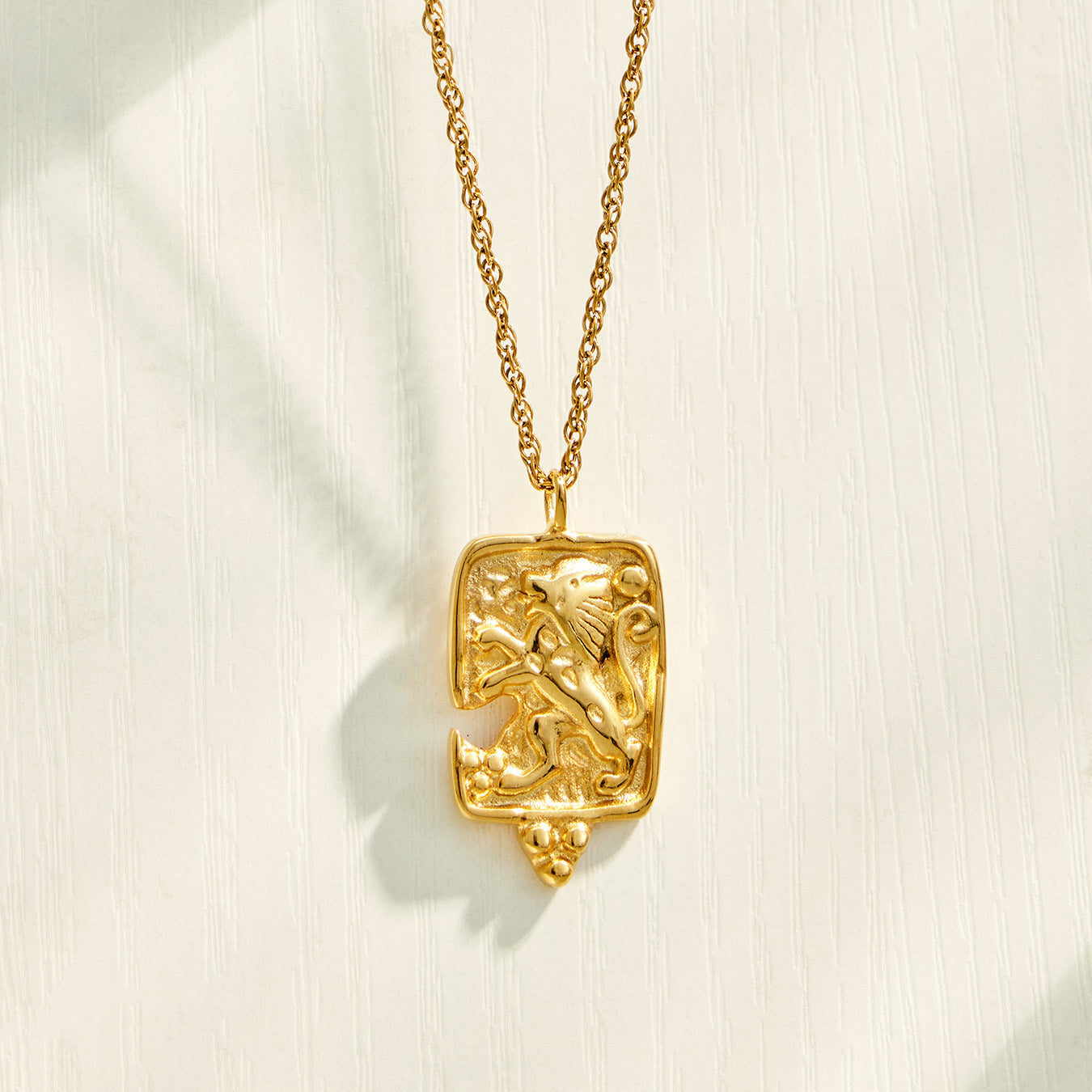 Close-up of the sculpted relief surface on a gold rectangular pendant necklace