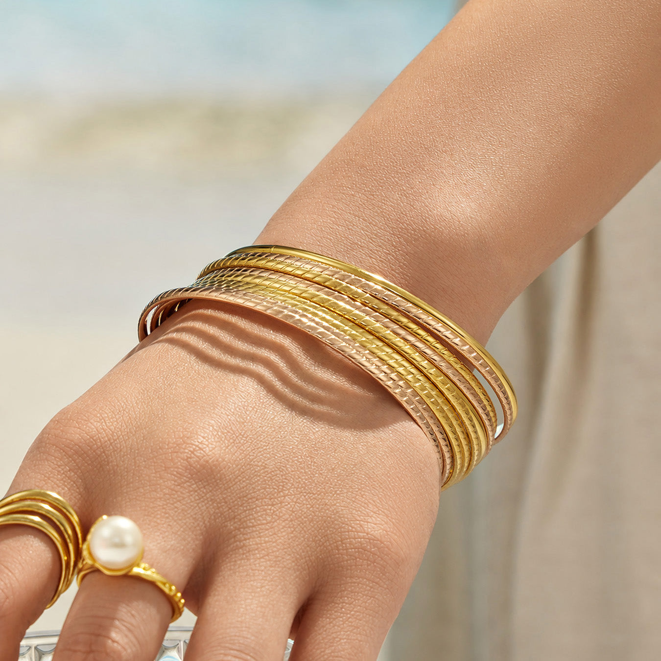Model wearing textured gold and rose gold-tone stackable bangles