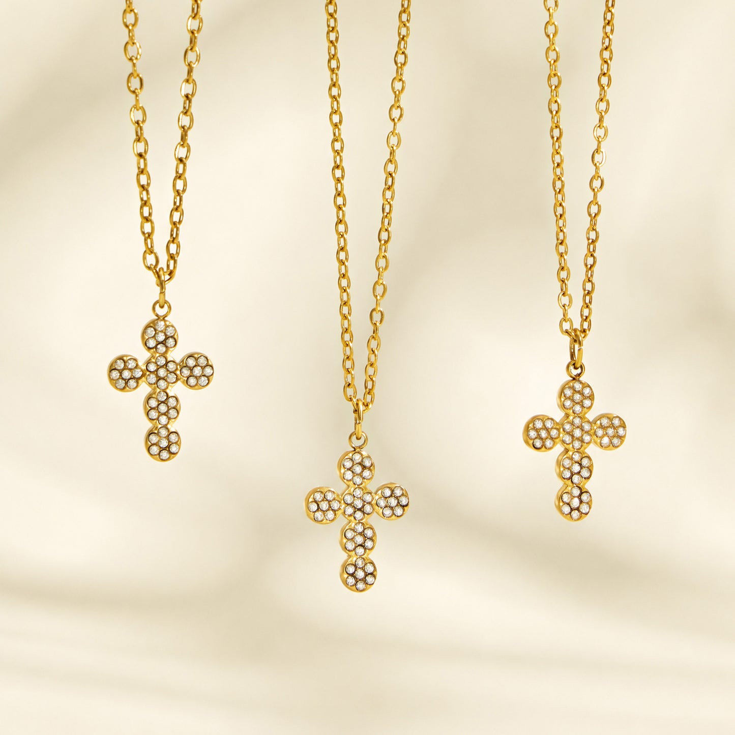 Three gold cross pendant necklace designs displayed vertically on a cream background