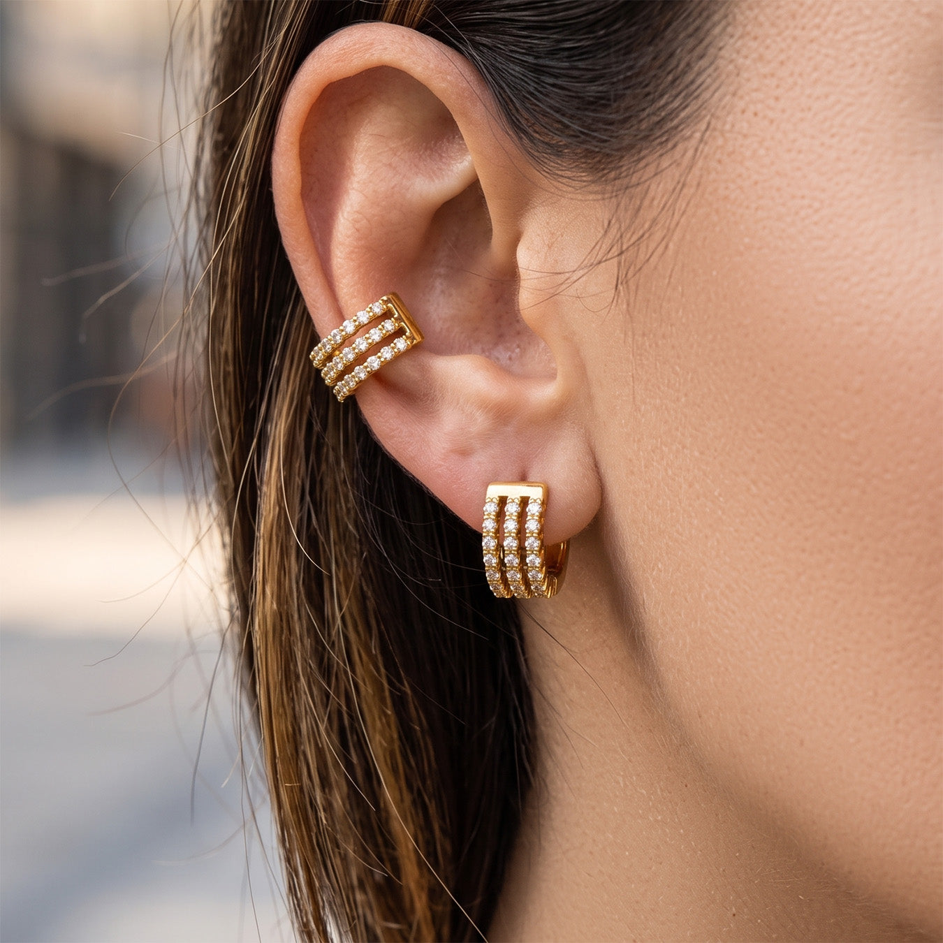 Side ear view of a model wearing triple-row gold pavé huggie earrings