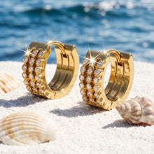 Close-up of gold triple-row huggie earrings in a coastal product setting