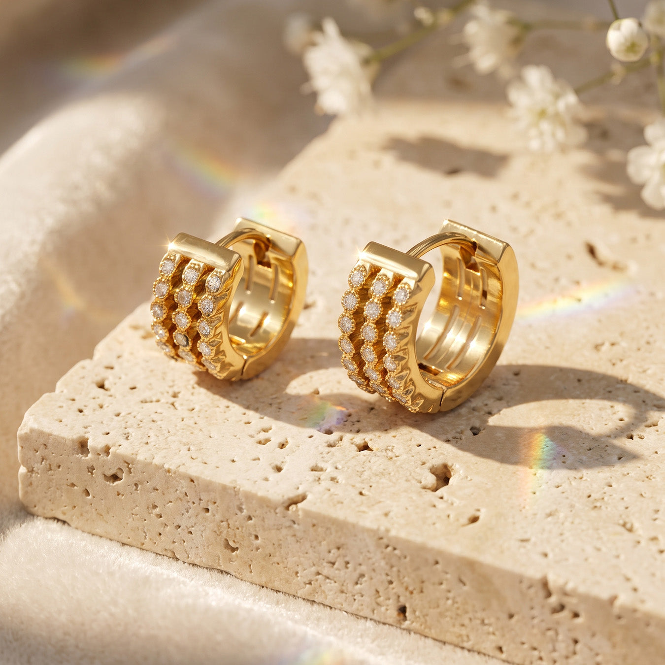 Triple-row zircon huggie earrings displayed on a light stone block with natural shadows
