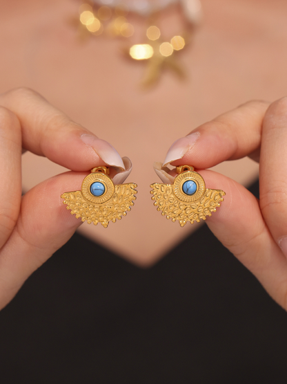 Close up of gold turquoise peacock fan stud earrings held beside model ear
