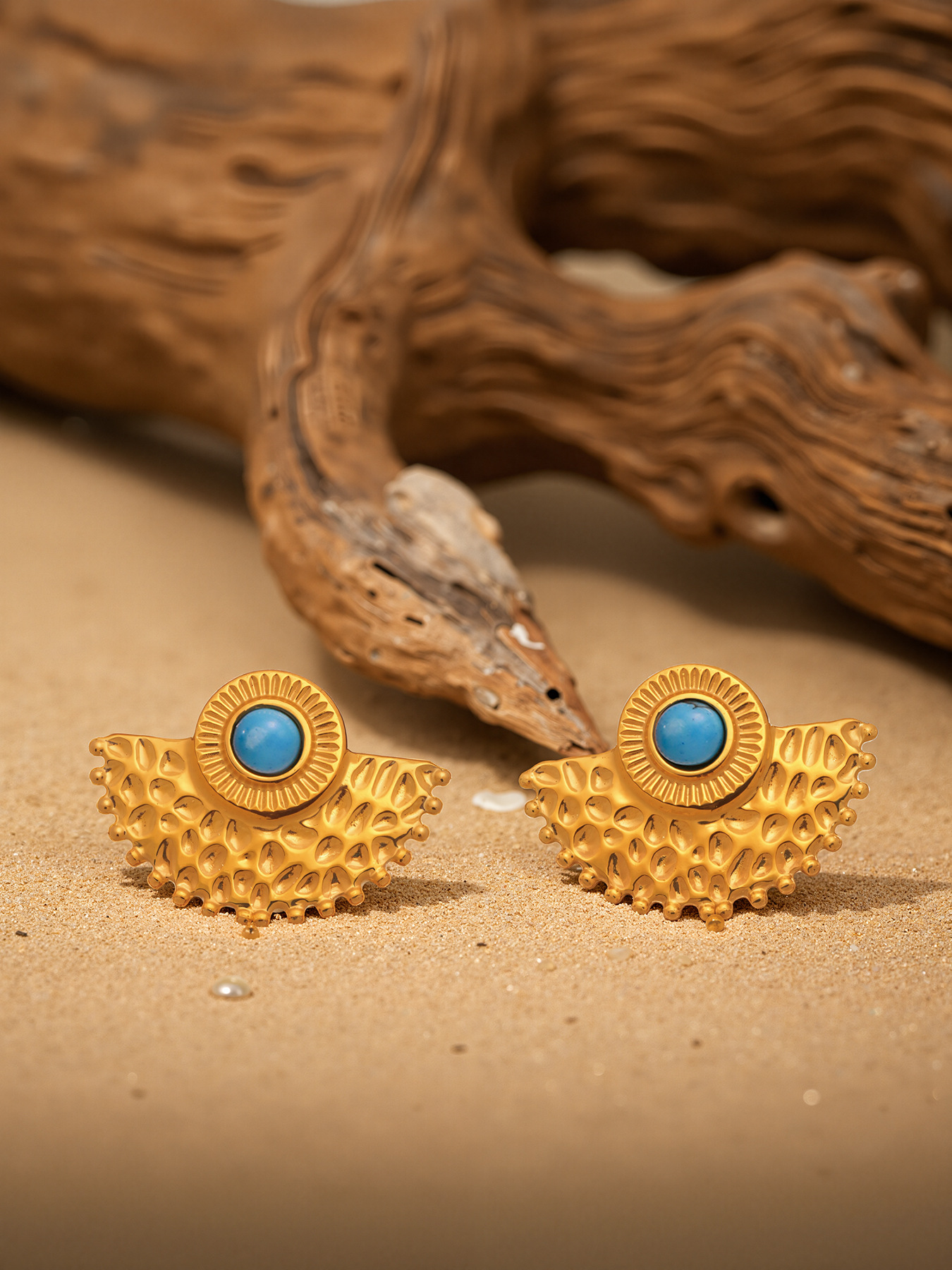 Turquoise peacock fan earrings displayed on sand with natural resort styling