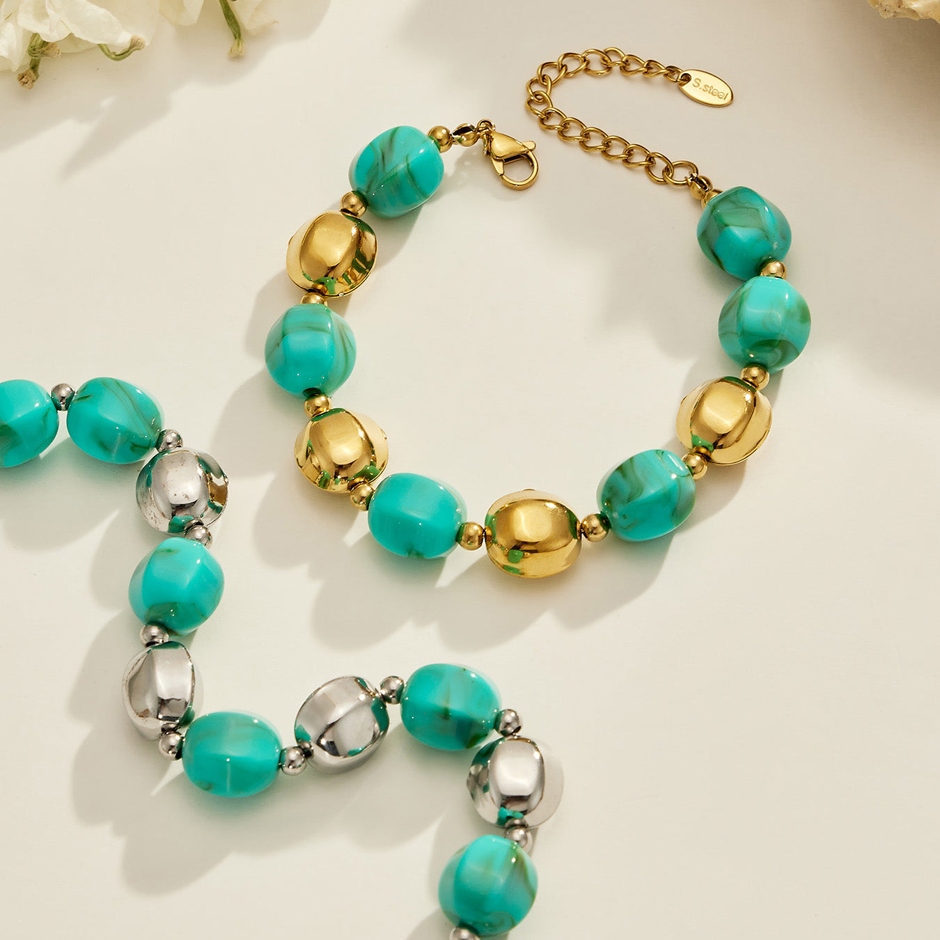Flat lay of a turquoise resin bead necklace and matching bracelet set with stainless steel accent beads.