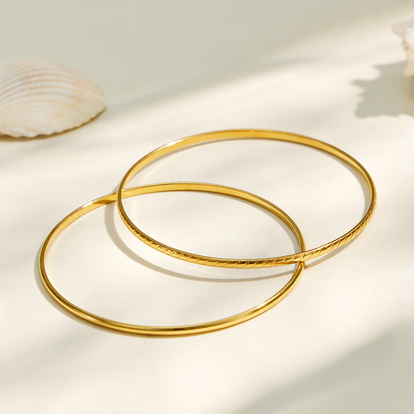 Two slim gold-tone stackable bangles arranged together on a light background
