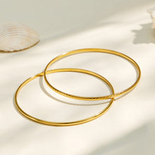 Two slim gold-tone stackable bangles arranged together on a light background