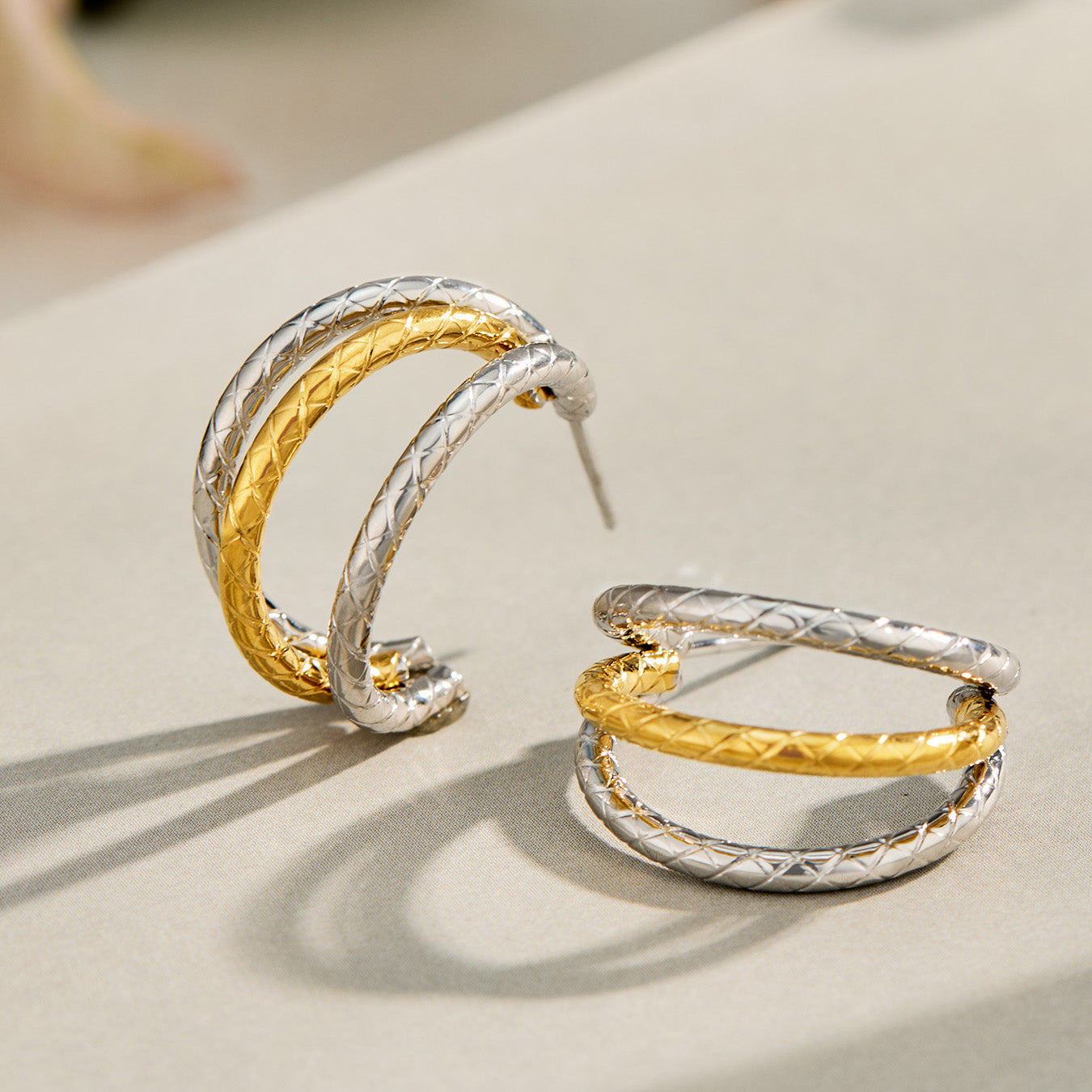 Gold and steel two-tone chunky C hoop earrings displayed on a light reflective surface