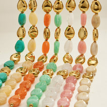 Colorful oval resin bead jewelry strands with polished gold-tone accents arranged in a vertical display