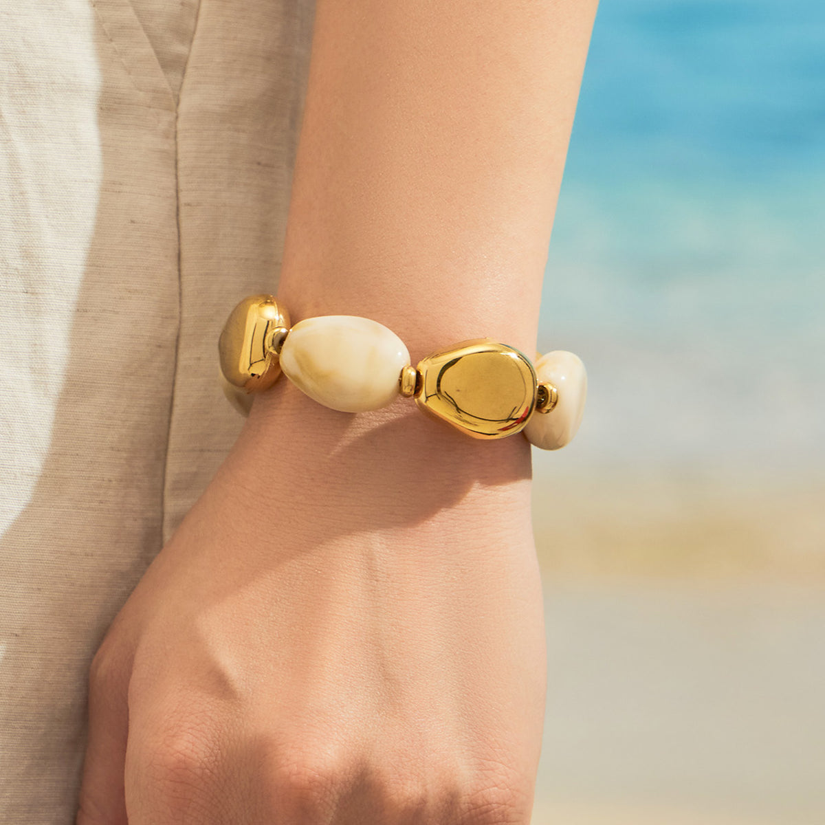 Close-up of a model wearing an ivory oval resin bead bracelet with polished gold-tone accents
