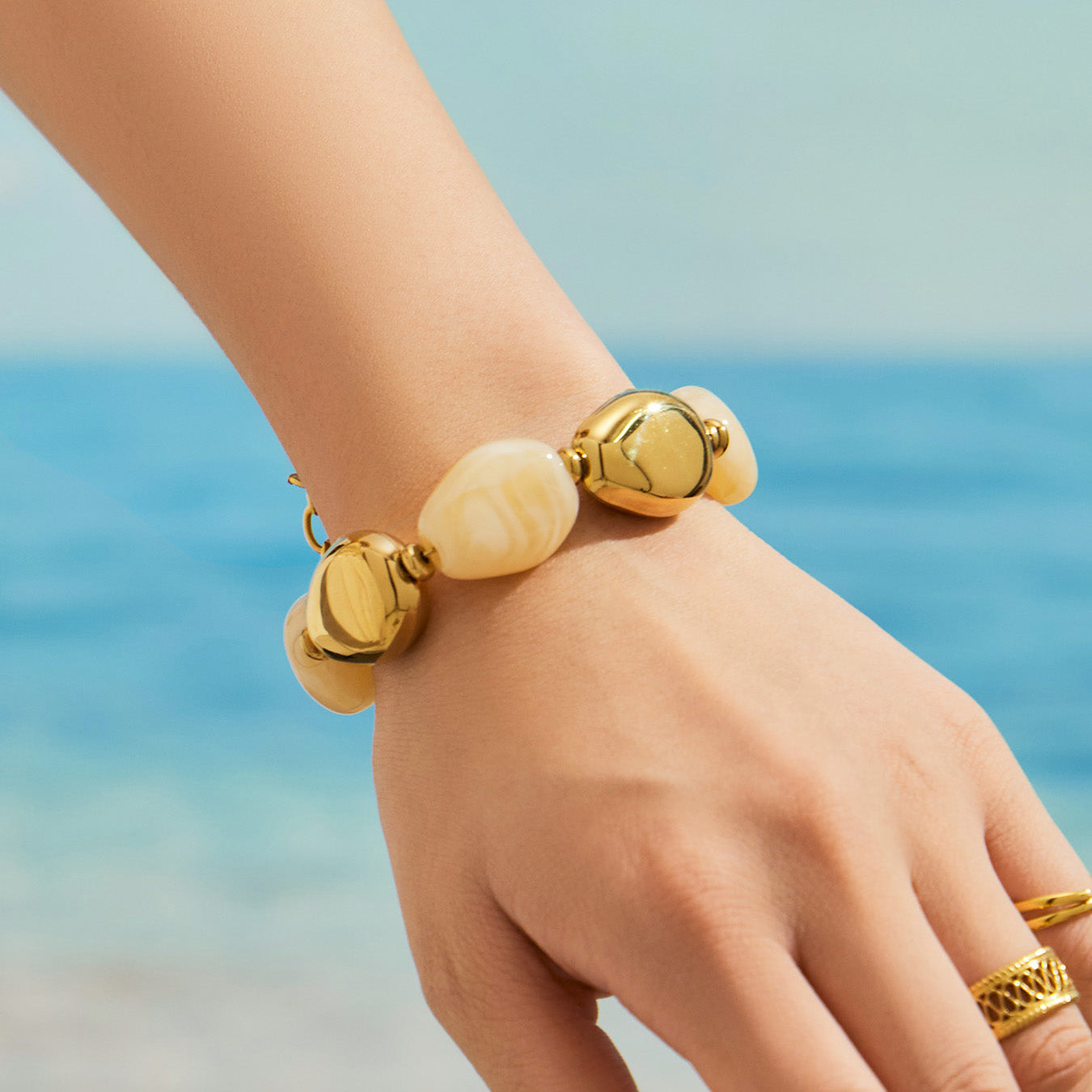 Ivory oval resin bead bracelet with gold-tone metal accents worn on a model wrist beside a blue background