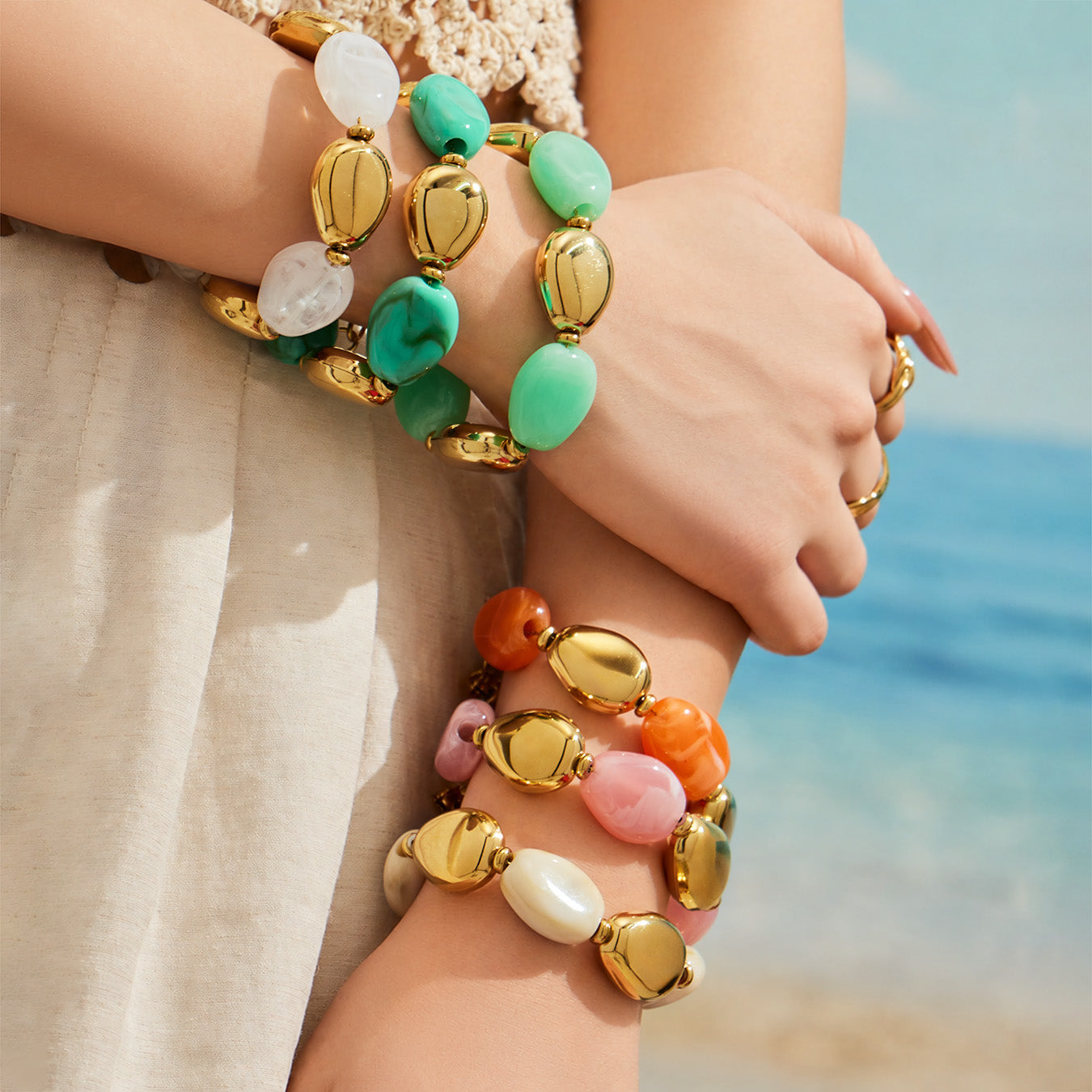 Model wearing stacked white green pink and orange-toned oval resin bead bracelets with gold-tone accents