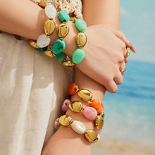 Model wearing stacked white green pink and orange-toned oval resin bead bracelets with gold-tone accents