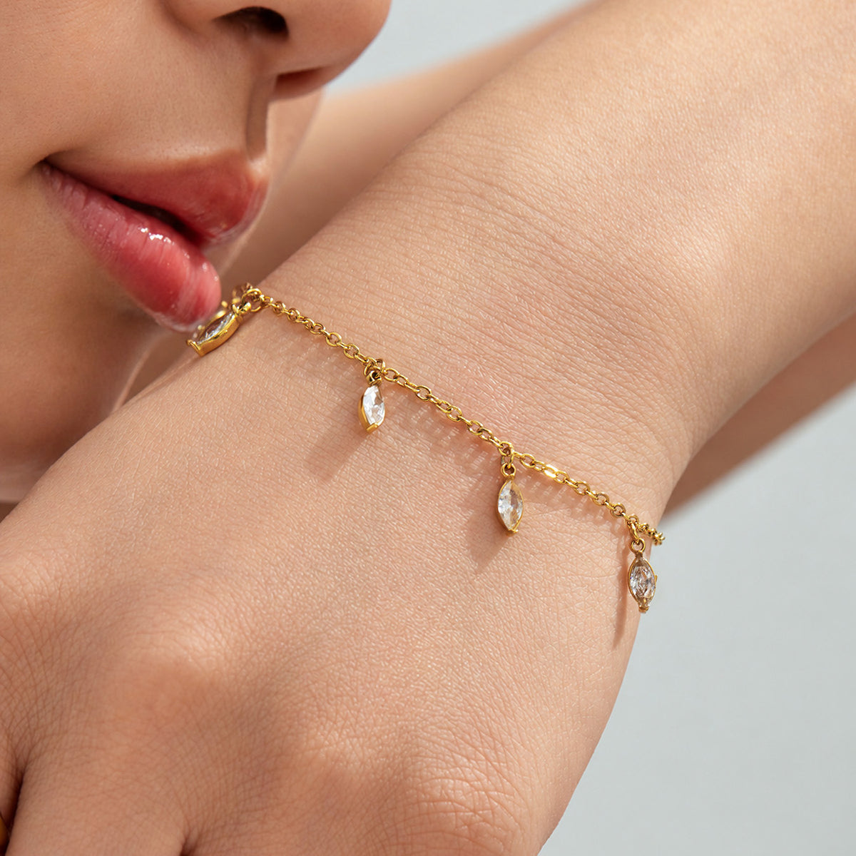 Close-up of a delicate gold-tone chain bracelet with small pointed teardrop charms worn on a wrist.