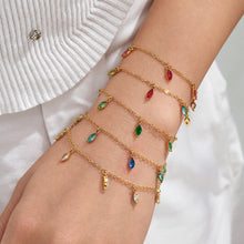 Several gold-tone chain bracelets with red, green and blue teardrop charms styled together on a wrist.