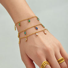 Layered gold-tone teardrop charm bracelets worn on a hand accessorized with several gold rings.