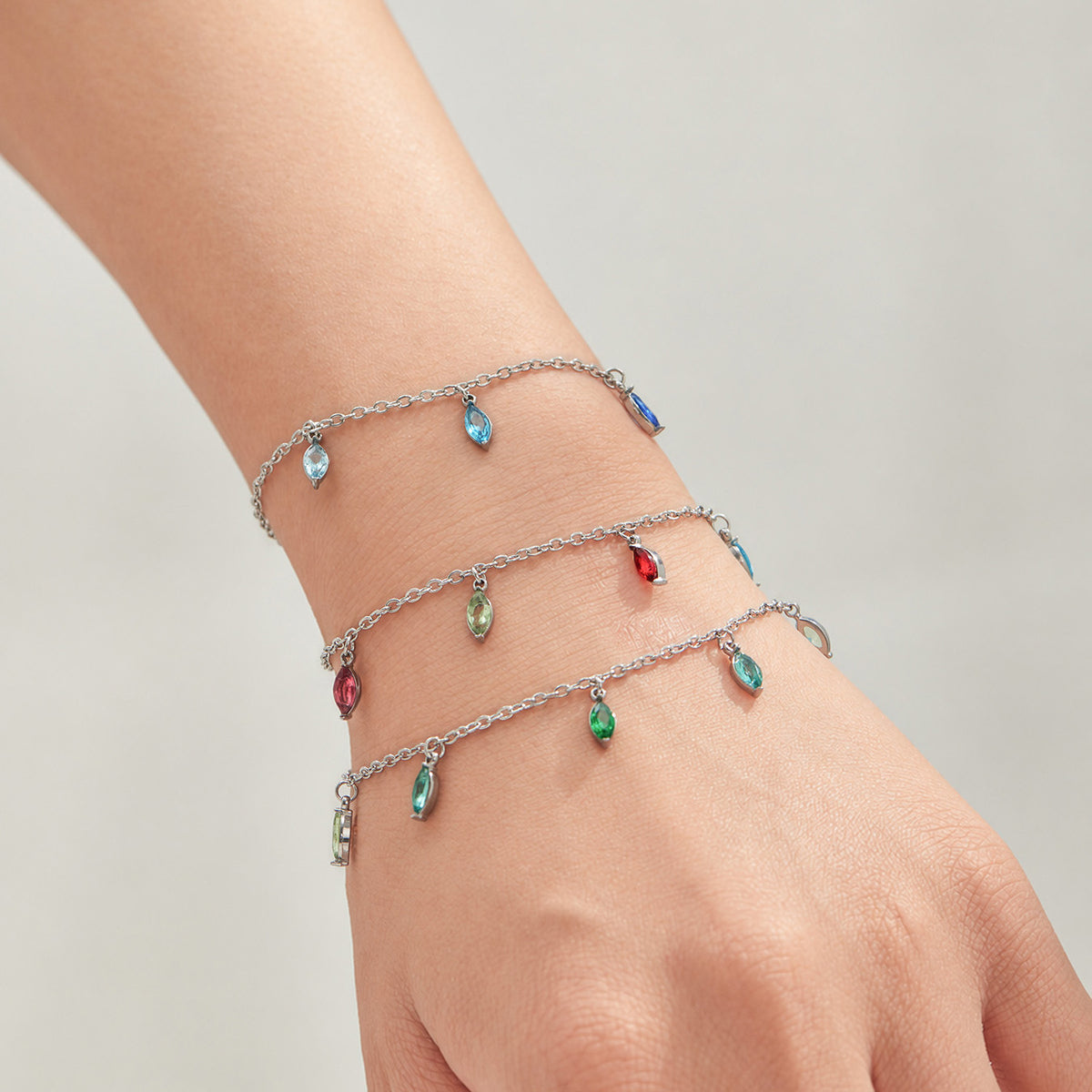 Layered steel-tone chain bracelets with colorful pointed teardrop charms worn on a wrist.