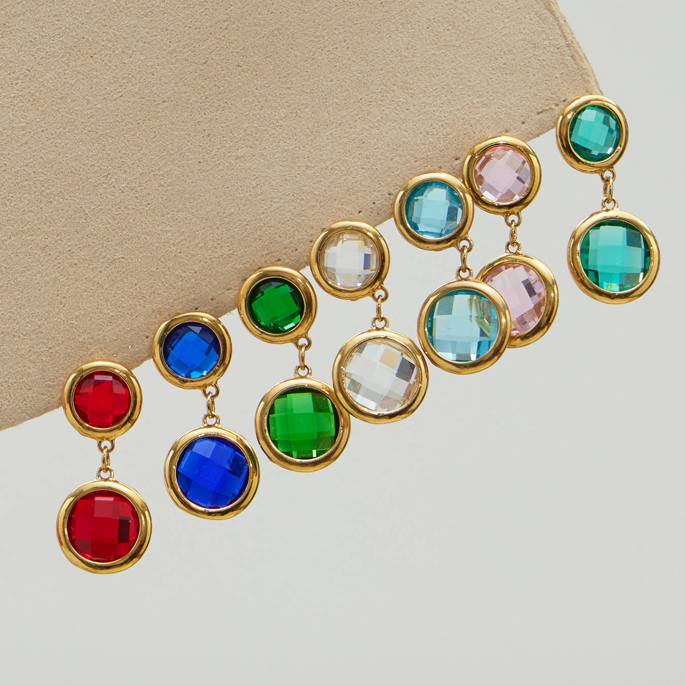 Double drop glass stone earrings in assorted colors on display, gold tone setting