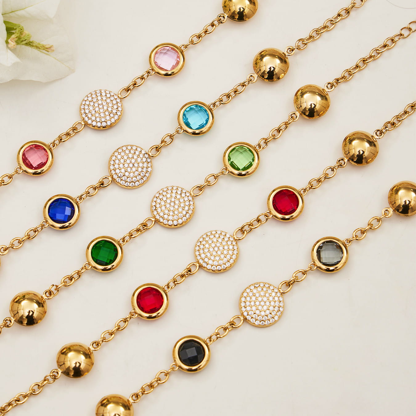 Stainless steel chain bracelet with pavé disc charm and colored glass stone stations, flat lay