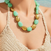 Model wearing a light green oval resin bead necklace with polished gold-tone accents and a crocheted top