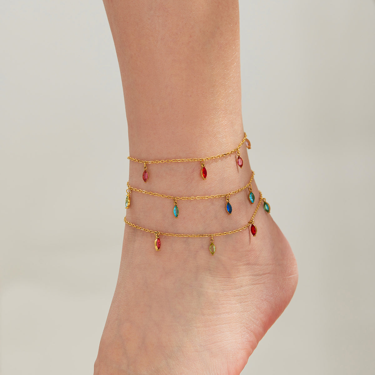Gold-tone anklets with small red, green and blue teardrop charms layered around an ankle.