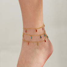 Gold-tone anklets with small red, green and blue teardrop charms layered around an ankle.
