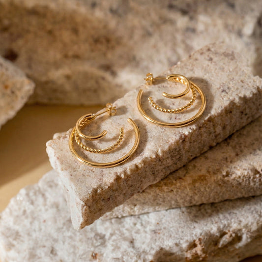 Aesthetic lifestyle photography of twisted rope gold earrings on natural stone texture.