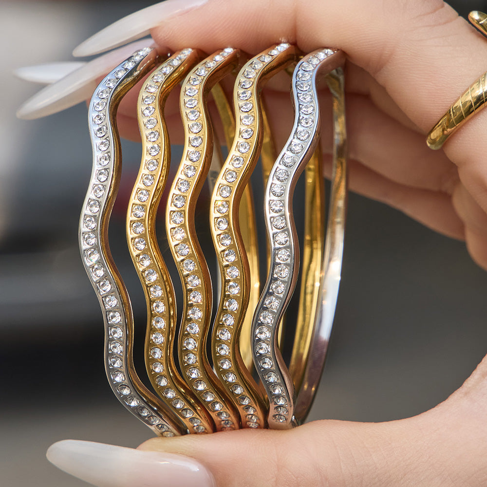 Hand holding gold and steel wavy zircon bangle bracelets with clear zircon accents, 316L stainless steel wholesale bracelet collection