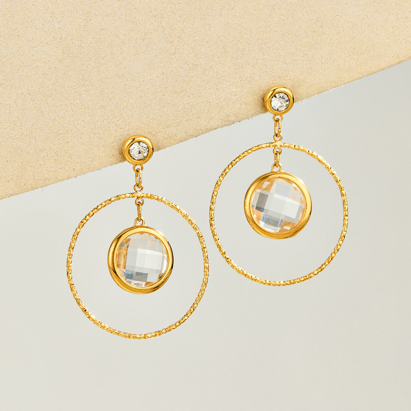 White glass stone drop earrings displayed with twisted gold-tone hoops