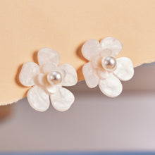 Flat lay of white flower pearl earrings on warm neutral background