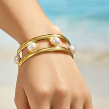 Wide gold cuff bracelet with pearl accents worn on a model wrist outdoors