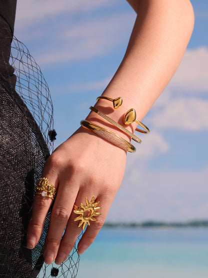 zircon paved slender bangle model lifestyle photo - stacked gold bangles on wrist with beach background
