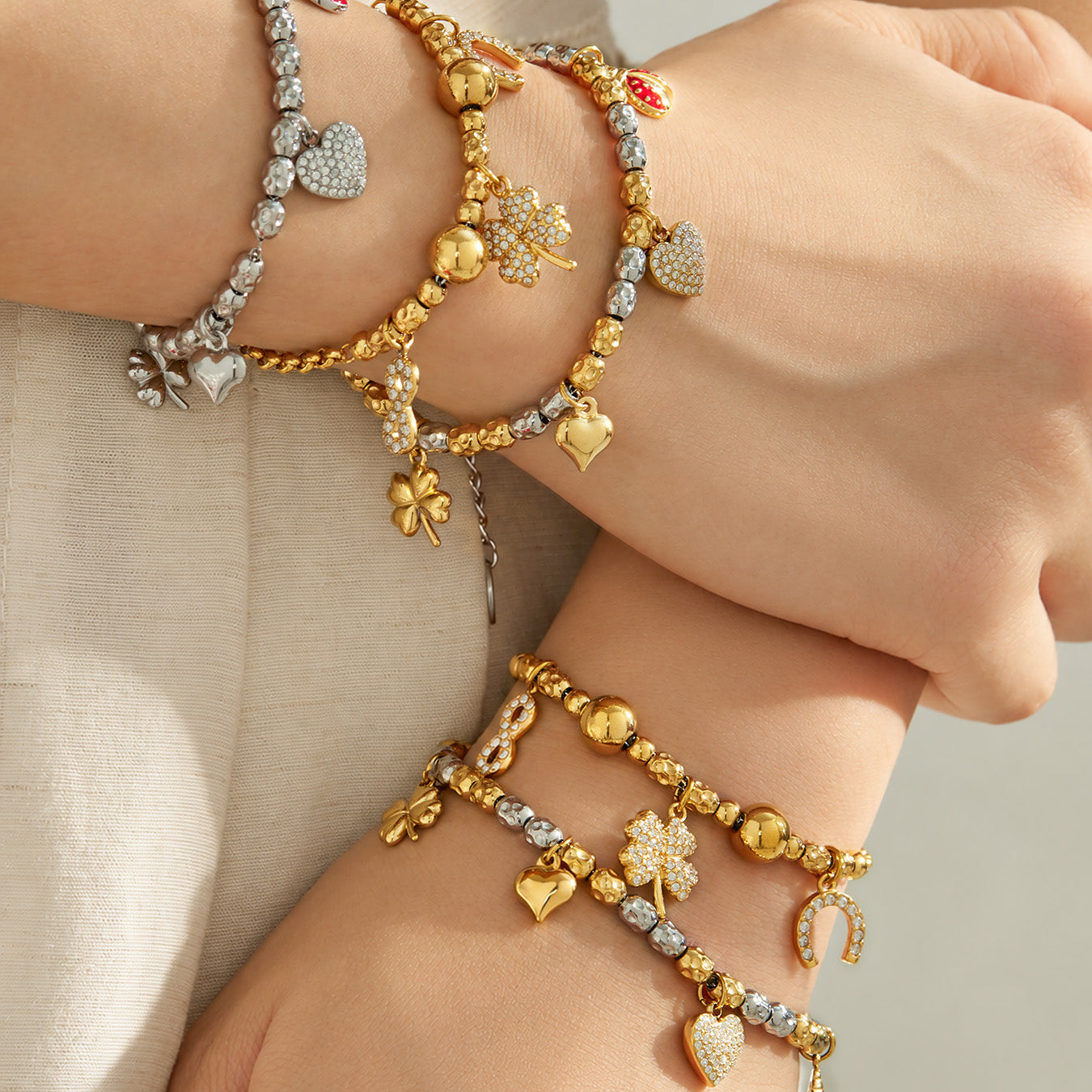 Gold and steel multi charm bracelets layered on the wrists with heart and decorative pendants