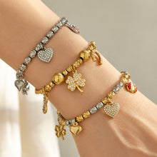 Gold and steel charm bracelets layered on the wrist with heart, horseshoe and colorful details